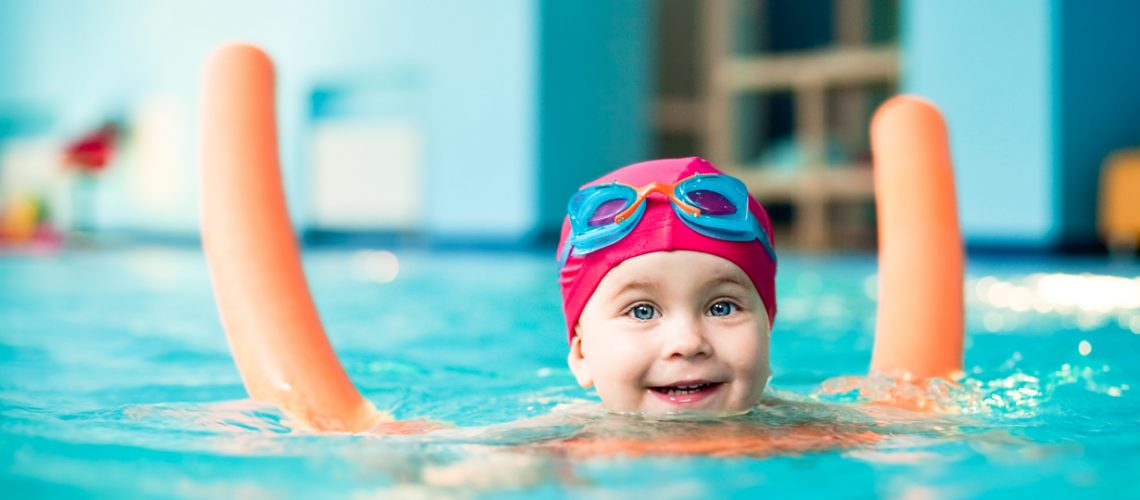 Happy little girl learning to swim with pool noodle