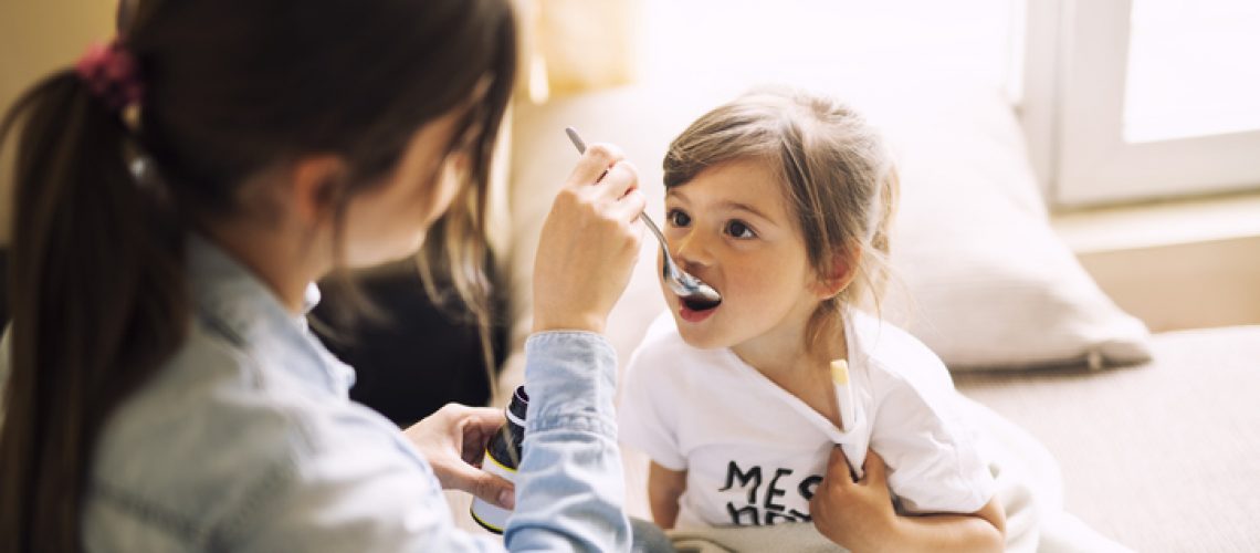 Mother giving daughter medicine on her sick daughter