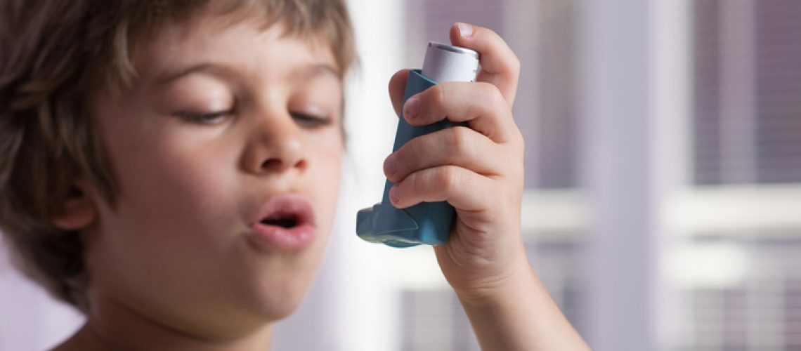 Boy using asthma inhaler to treat inflammatory disease, wheezing, coughing, chest tightness and shortness of breath. Allergy treating concept. Selective focus on inhaler.